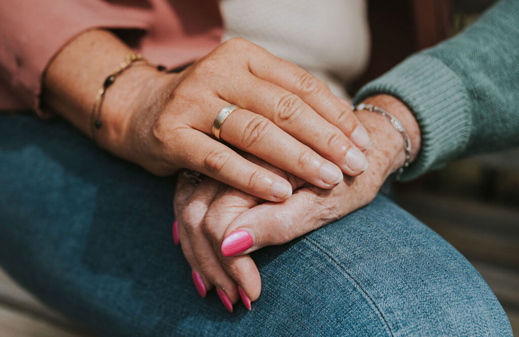 Hand van de verzorger houdt de hand van de oudere met dementie vast